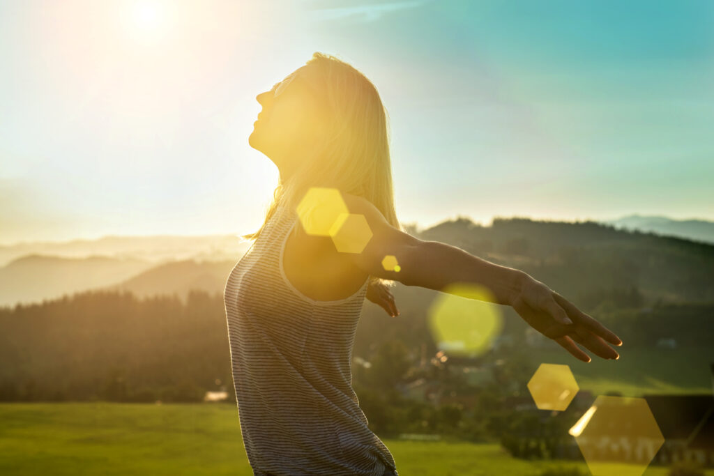 Happy woman with open arms stay on the peak of the mountain cliff edge under sunset light sky enjoying the success, freedom and bright future.